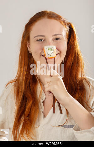 Divertimento ragazza con rotolo di sushi su sfondo bianco sorridente guardando la telecamera visualizza naso Foto Stock