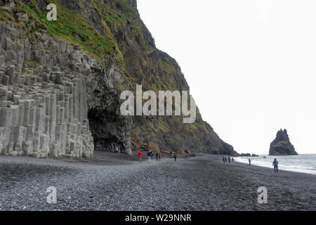 Vista lungo la spiaggia verso il esagonale a colonne di basalto Reynisfjara sulla spiaggia di sabbia nera, sud dell'Islanda. Foto Stock