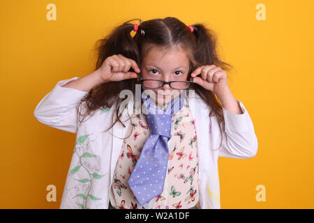 Signor - Scienza Geek giovane ragazza / femmina in bicchieri di 7 anni - il bambino scienziato guardando sopra gli occhiali a fotocamera su sfondo giallo Foto Stock