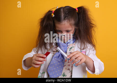 MR - esperimento scientifico a casa Geek Child Glasses età 7 concentrandosi sulla miscelazione di sostanze chimiche liquide in provette su sfondo giallo con spazio di copia Foto Stock