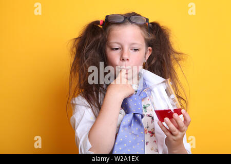 Signor - Scienza Geek giovane ragazza / femmina - 7 anni - bambino degustazione liquido rosso da una scienza di borosilicato becher su sfondo giallo Foto Stock