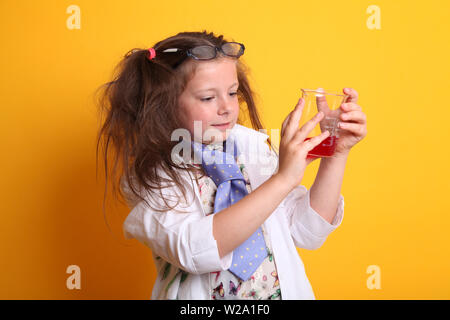 Signor - Scienza Geek giovane ragazza / femmina - 7 anni - bambino misurazione liquido rosso in una scienza di borosilicato becher su sfondo giallo Foto Stock