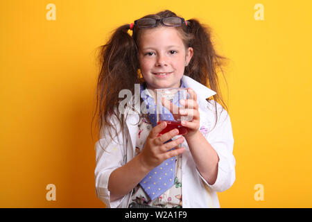 Signor - Scienza Geek giovane ragazza / femmina - 7 anni - bambino sorridente in telecamera tenendo la scienza di borosilicato becher di prodotti chimici di colore rosso su sfondo giallo Foto Stock