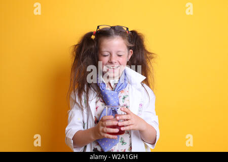 Signor - Scienza Geek giovane ragazza / femmina - 7 anni - bambino ridere per fotocamera, gli occhi chiusi, tenendo in borosilicato scienza becher su sfondo giallo Foto Stock