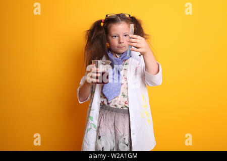 Signor - Scienza Geek giovane ragazza / femmina - 7 anni - bambino controllare le misurazioni in un tubo di prova tenendo in borosilicato scienza becher su sfondo giallo Foto Stock