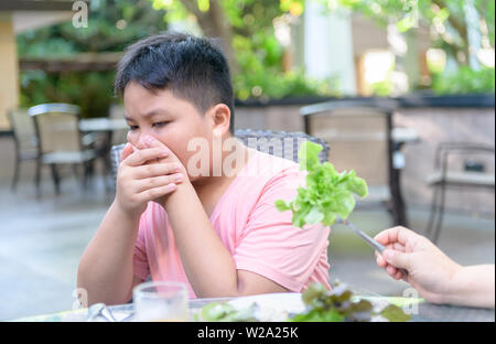 Obesi Fat Boy con espressione di disgusto contro le verdure in insalata, rifiutando il concetto di cibo Foto Stock