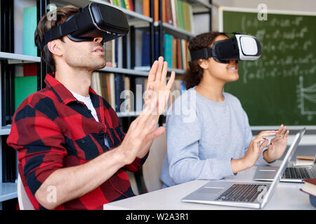 Il giovane e il suo compagno di classe in occhiali vr toccando il display virtuale Foto Stock