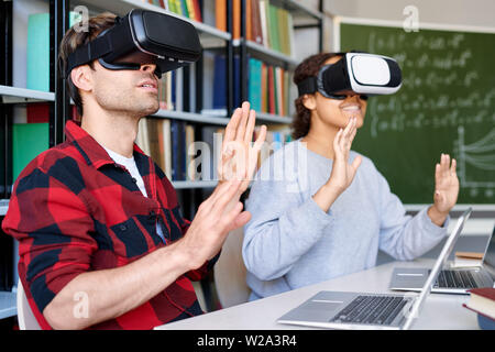 Due stupiti i compagni di scuola in occhiali vr toccando roba virtuale Foto Stock