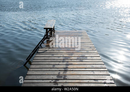 Bella molo in legno con panca e sun riflette sulla calma e acqua blu Foto Stock