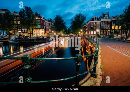 Serata in città di Amsterdam, sentieri di luce e di riflessi sull'acqua a Leidsegracht e Keizersgracht canali. Una lunga esposizione shot. Viaggio di città in visita Foto Stock