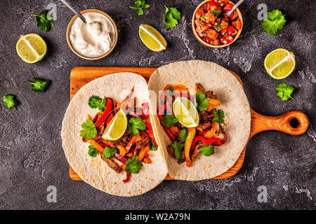 Le FAJITAS colorato con pepe e cipolle, servita con tortillas, salsa e panna acida. Foto Stock