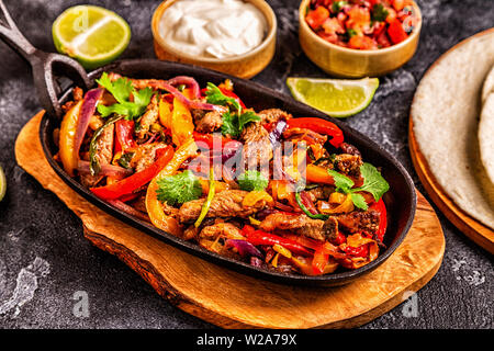 Le FAJITAS colorato con pepe e cipolle, servita con tortillas, salsa e panna acida. Foto Stock