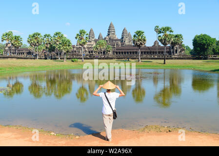 Un turista in visita a Angkor Wat rovine presso sunrise, meta di viaggio Cambogia. Donna con cappello tradizionale e bracci sollevati, vista posteriore, facciata principale refl Foto Stock