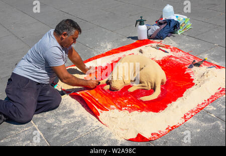 Maschio maturo artista che lavora su una statua di sabbia di un sonno cane in Liverpool Foto Stock