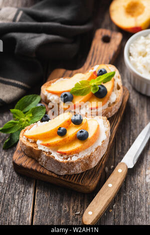 Bruschetta con ricotta, di pesche e mirtilli su sfondo di legno Foto Stock