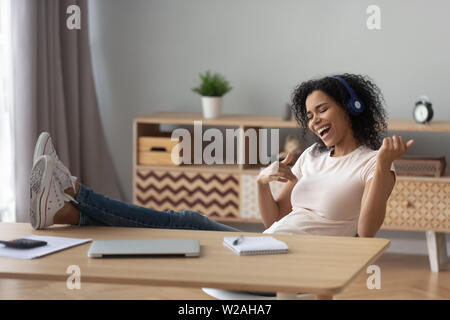 Felice donna africana indossare le cuffie a suonare la chitarra per rilassarsi dopo il lavoro Foto Stock