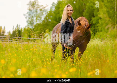 Donna sorridente alimentando il suo cavallo arabo amico con spuntini nel campo Foto Stock