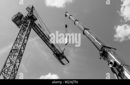 Gru a torre di assemblaggio. Contrappeso in calcestruzzo l'installazione. Artistico in bianco e nero skyline. Erezione di dispositivo di sollevamento costruzione. Il braccio telescopico. Foto Stock