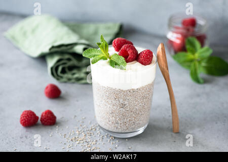 Budino di Chia con strato di yogurt e lamponi freschi in un vetro sul cemento grigio nella tabella. Pulire mangiare, dieta e perdita di peso concept Foto Stock