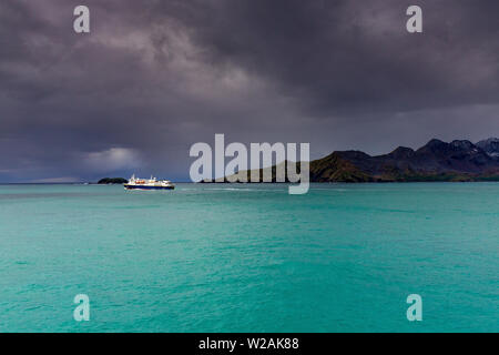 Vista della nave a vela da Cumberland Bay Georgia del sud. Dark nuvole temporalesche sopra ma la luce del sole sullo splendido mare turchese Foto Stock