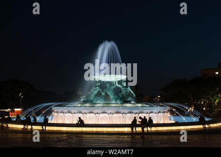 Persone da rilassanti i tritoni fontana all'entrata a La Valletta, Malta, illuminata di notte Foto Stock