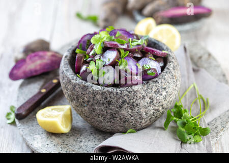 Chilotan cilena cucina isolana. Viola Viola insalata di patate con il limone, molla di cipolla e il coriandolo nella ciotola in pietra. Sfondo grigio. Foto Stock