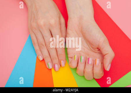 Elegante e moderno con manicure arcobaleno o estate umore, su una tabella di colore rosa con buste colorate vista superiore Foto Stock