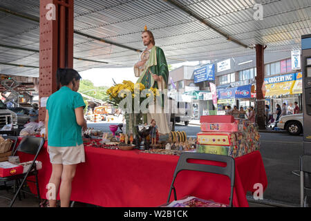 Una donna si ferma a fare acquisti in un stand esterno che vende articoli religiosi. A Roosevelt Ave. sotto la metropolitana sopraelevata in Elmhurst, Queens, a New York. Foto Stock