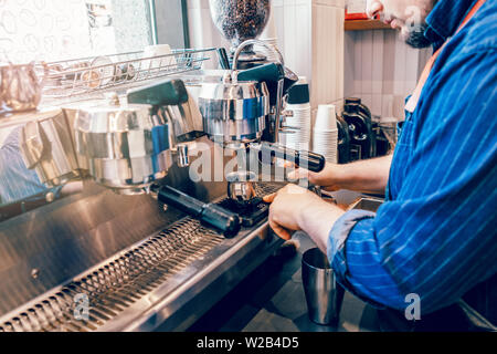 Caucasian barista uomo rendendo il caffè fresco espresso cappuccino. Server versando una bevanda calda dalla macchina professionale per brocca in metallo in piedi su piccola scala Foto Stock