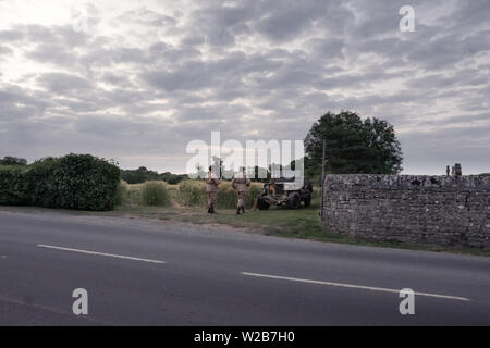 Due uomini vestiti in Guerra Mondiale 2 uniformi nei pressi di un vintage jeep dal lato della strada e la preparazione per una rievocazione storica Foto Stock