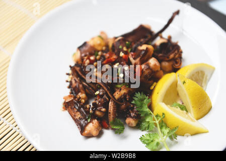 Insalata di Polpo con limone erbe e spezie su piastra bianca / tentacoli di calamari alla griglia cibo antipasto caldo e peperoncino piccante salsa a base di pesce serviti cotti Foto Stock