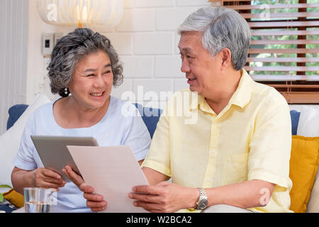 Asian coppia senior utilizzano tablet ricerca sulla pensione documento finanziario seduti sul divano di casa,senior imparare a utilizzare la tecnologia.affinamento in luogo con Foto Stock