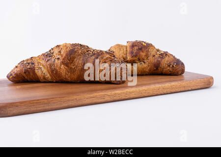 Due croissant appena sfornati con semi di sesamo su un isolato scheda di taglio su uno sfondo bianco. Foto Stock