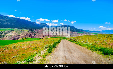 Strada di ghiaia in irriguo fertili terreni agricoli lungo il fiume Fraser come fluisce attraverso il canyon alla città di Lillooet in BC di interni in Canada Foto Stock