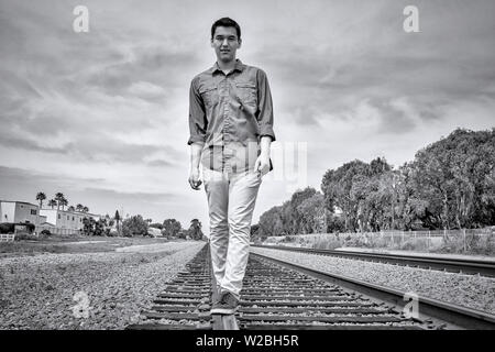 Giovane uomo a camminare su binari ferroviari a Carlsbad, California Foto Stock
