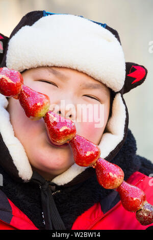 Cina, Provincia di Heilongjiang, Harbin, Central shopping street, ragazzo di mangiare frutta congelata in inverno Foto Stock