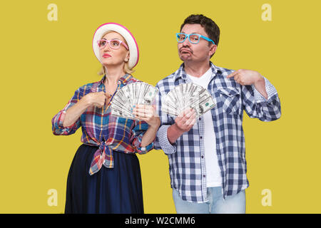 Paio di certi amici, adulto uomo e donna casual in camicia a scacchi in piedi insieme mantenendo la ventola di dollari e le dita di puntamento a se stesso w Foto Stock
