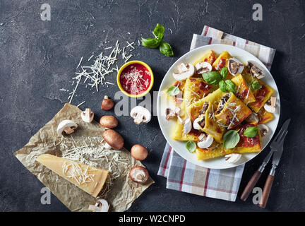 Crêpe rotoli con funghi e parmigiano ripieno su una piastra bianca su una tabella di calcestruzzo con salsa di pomodoro e un pezzo di formaggio e di asciugatutto, vista da un Foto Stock