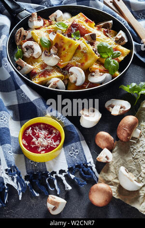 Deliziosa crepes con funghi e parmigiano ripieno su una padella su una tabella di calcestruzzo con salsa di pomodoro e di asciugatutto, vista verticale Foto Stock