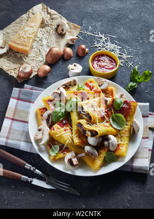 Rotoli di crepes con funghi e parmigiano ripieno su una piastra bianca su una tabella di calcestruzzo con salsa di pomodoro e un pezzo di formaggio, vista verticale da sopra Foto Stock