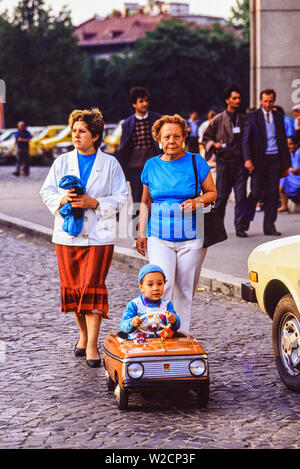 Bucarest, Romania. Maggio 1990. Due donne a piedi dietro un bambino in una macchina giocattolo. Foto: © Simon Grosset. Archivio: immagine digitalizzati da un originale di trasparenza. Foto Stock