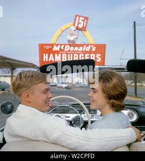 Il fast food negli anni cinquanta. Una giovane coppia nella loro autovettura convertibile con un McDonald's sign in background. Il giallo arch facente parte del progetto originale chiamato il Golden Arches è stato utilizzato per la prima volta 1953. Il costo di un menu limitato hamburger, agitare e patatine fritte era di 15 centesimi. Anni Cinquanta anni sessanta ref 5-40-4 Foto Stock