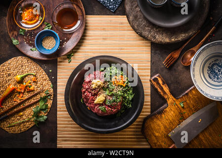 Carni macinate in nero ciotola con un trito di aglio, peperoncino, Zenzero e erbe su cucina scuro sfondo tabella con sesamo e salsa di soia in ciotole, vista dall'alto. St Foto Stock