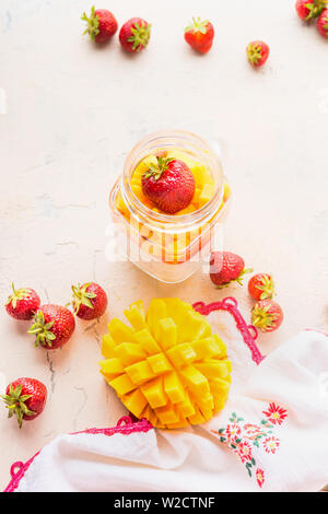 Mango e fragole con budino di yogurt in un barattolo di vetro sul tavolo bianco. Close up. Una sana prima colazione Foto Stock