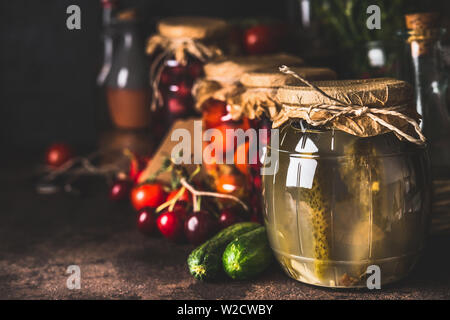 Varie fermentato conserve di verdure di stagione e frutta dal giardino in vasetti di vetro scuro su sfondo rustico, vicino. Autunno Canning. Conservazione Foto Stock