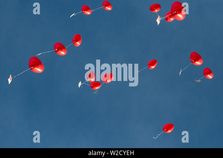 Più rosso a forma di cuore palloncini in volo, naturale blu cielo Foto Stock