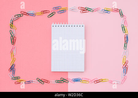 Notebook in gabbia in una cornice di carta colorata clip su un duplice sfondo - rosa e corallo. Concetto torna a scuola. Foto Stock