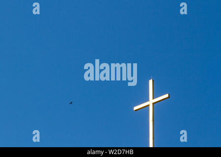 Croce luminosa sulla parte superiore del campanile di Santo Stefano chiesa con un flying swallow contro il cielo blu a Sopron, Ungheria Foto Stock