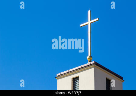 Croce luminosa sulla parte superiore del campanile di Santo Stefano Chiesa contro il cielo blu in Sopron, Ungheria Foto Stock