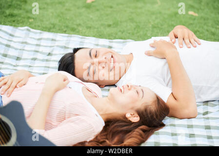 Giovani asiatici giovane giacente su una coperta sull'erba e ridere durante il loro riposo su picnic Foto Stock